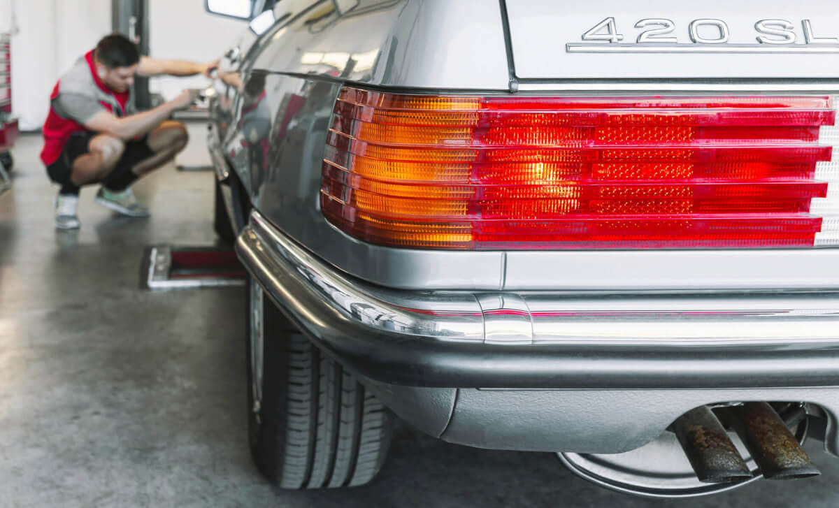 Mercedes Oldtimer Ein Mechaniker von GTÜ Neidhardt kontrolliertdie rechte Seite eines silbernen Oldtimer Mercedes 420 SL in einer Prüfstelle.