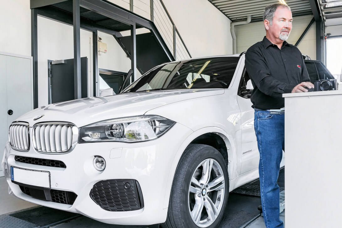 Leasing Rückläuferprüfung Ein Mitarbeiter von GTÜ Neidhardt steht an einem Prüfstand und bedient einen Computer, vor ihm steht ein weißes Auto.