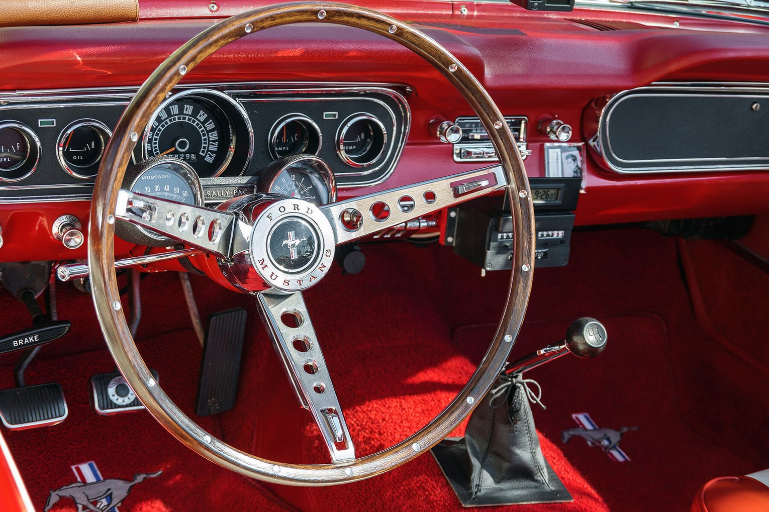 Ford Mustang Cockpit Innenraum eines roten Ford Mustang mit glänzendem Lenkrad, klassischen Rundinstrumenten und rotem Teppichboden.