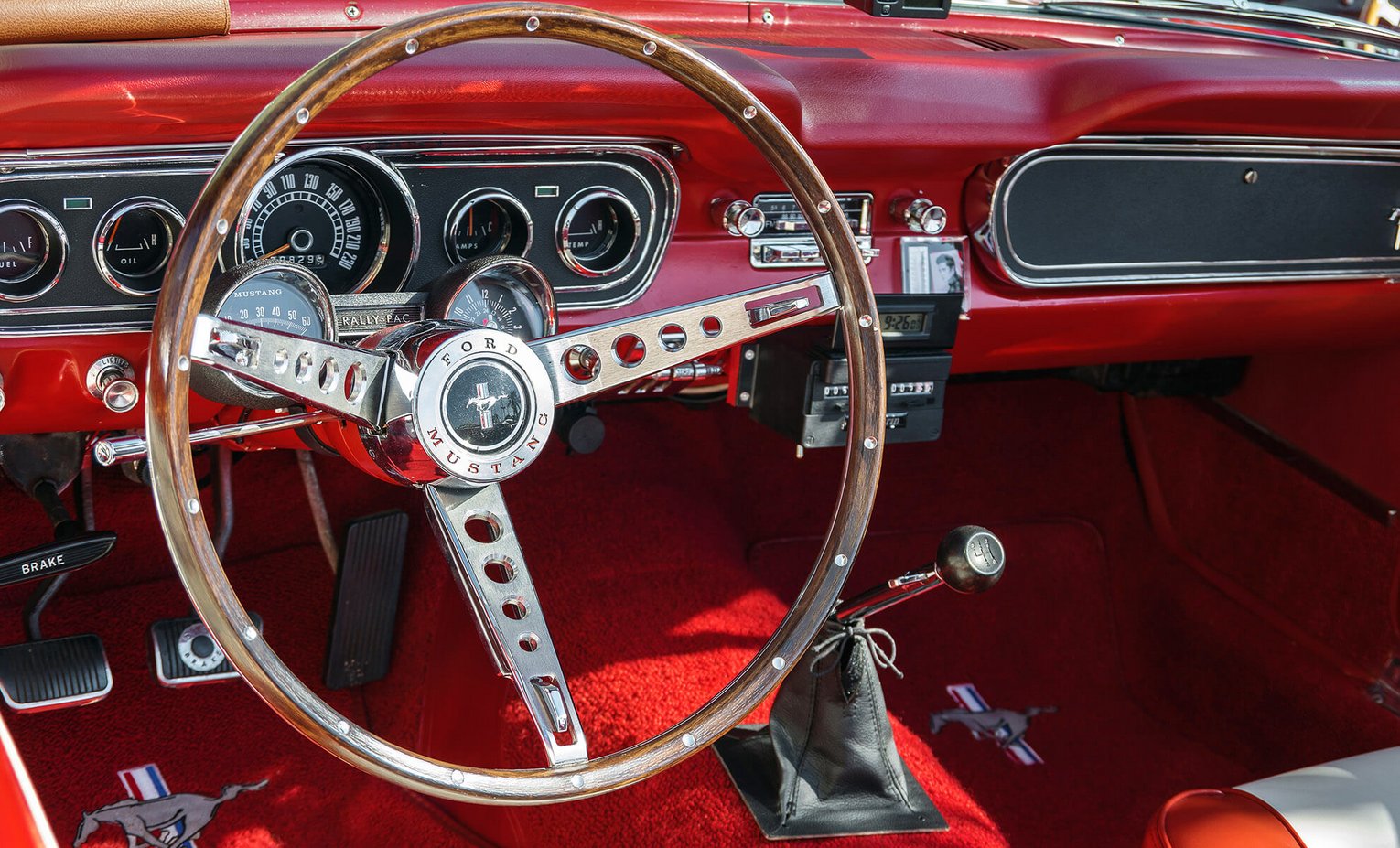 Ford Mustang Cockpit Innenraum eines roten Ford Mustang mit glänzendem Lenkrad, klassischen Rundinstrumenten und rotem Teppichboden.