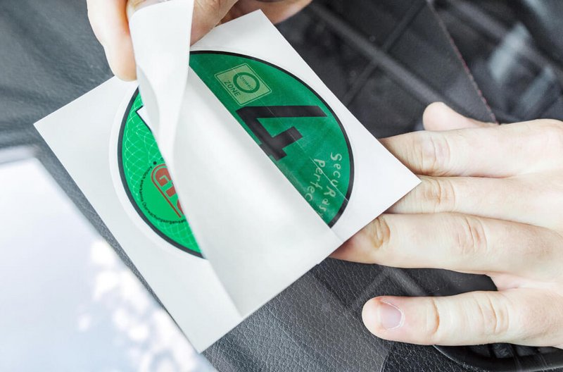Anbringung der Umweltplakette Hand klebt eine grüne Umweltplakette mit der Zahl 4 auf eine Windschutzscheibe.