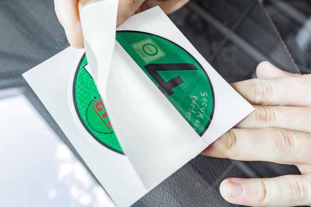 Hand klebt eine grüne Umweltplakette mit der Zahl 4 auf eine Windschutzscheibe.